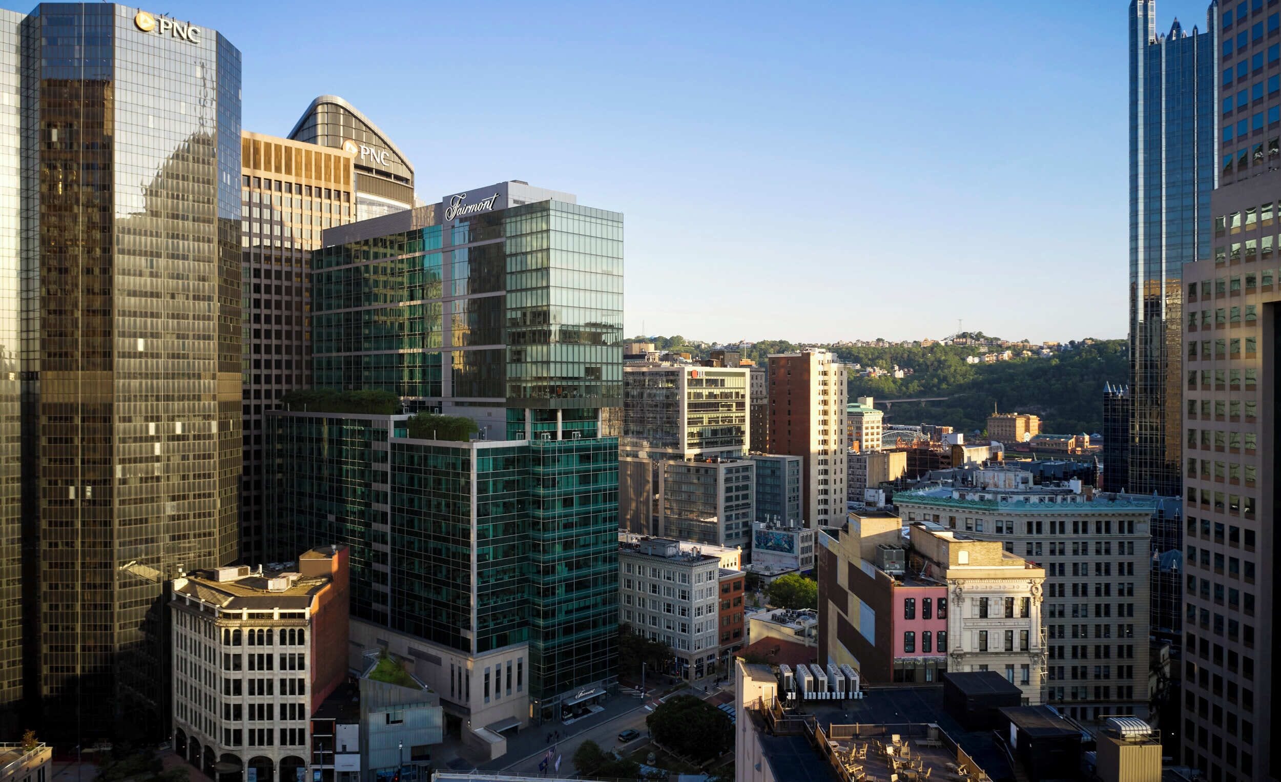 A cityscape with modern high-rise buildings, including a prominent glass building with a 'Fairmont' sign.