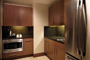 A kitchen with wooden cabinets, a stainless steel refrigerator, a built-in microwave, and a granite countertop. - Fairmont Pittsburgh (Pittsburgh)