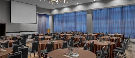Un salón de conferencias con mesas redondas, sillas y una pantalla grande.