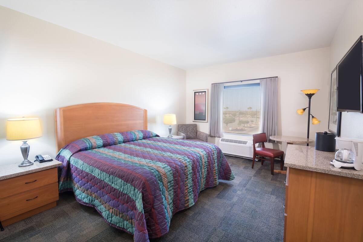 A hotel room with a bed, bedside tables, a desk, a chair, a window with curtains, and a view of the outdoors.