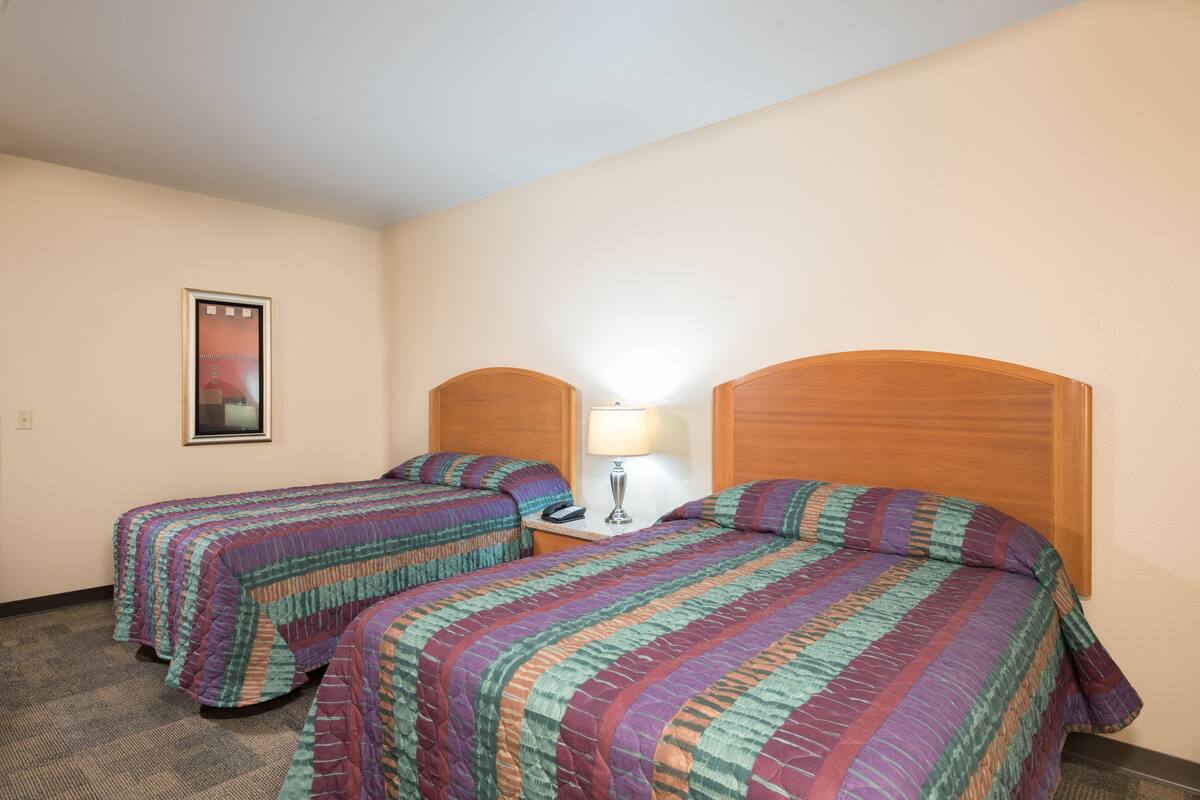 A hotel room with two beds, each with a colorful quilt, a nightstand with a lamp, and a framed picture on the wall.