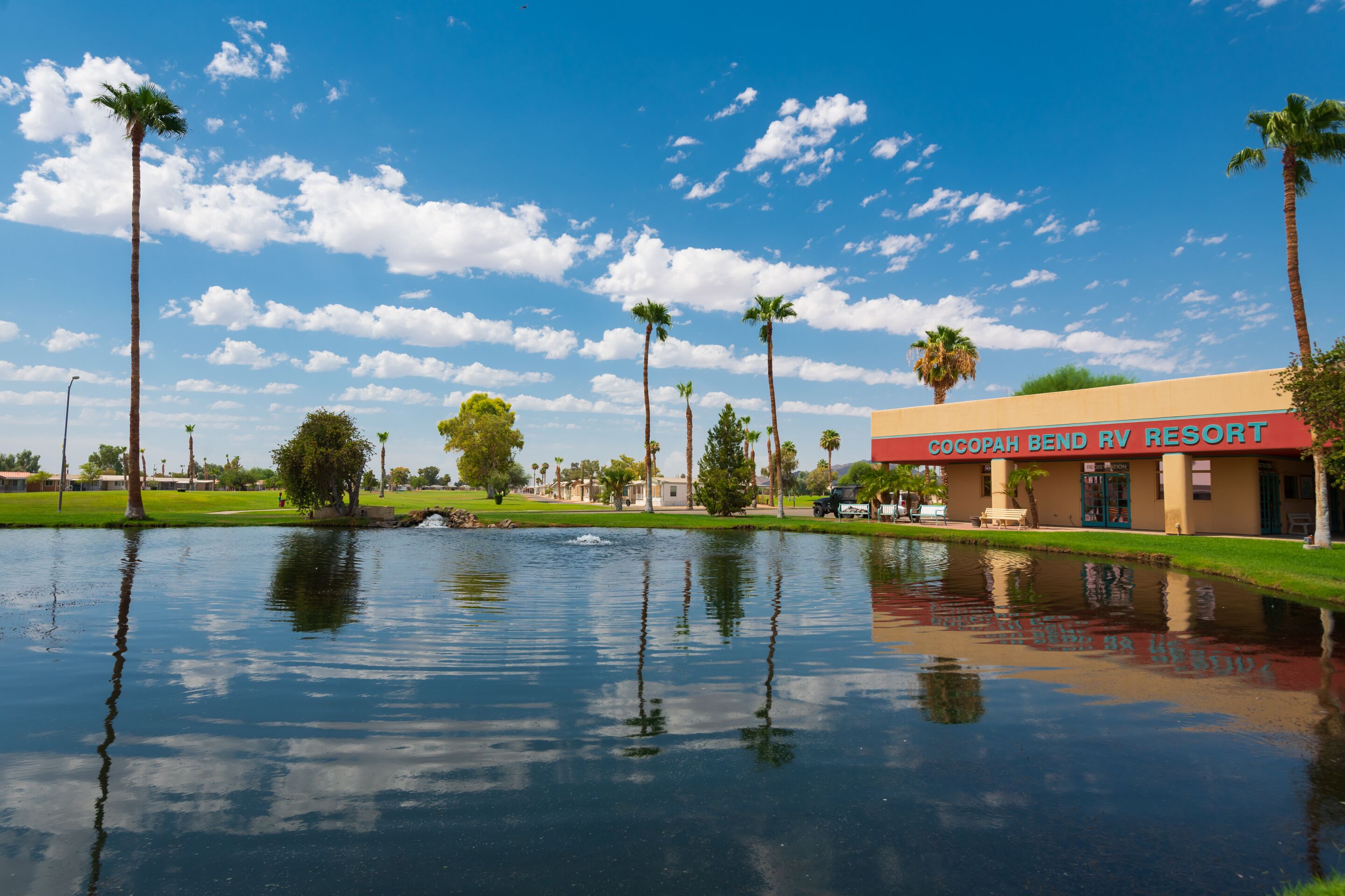 A resort with a water feature in front, palm trees, and a clear blue sky.