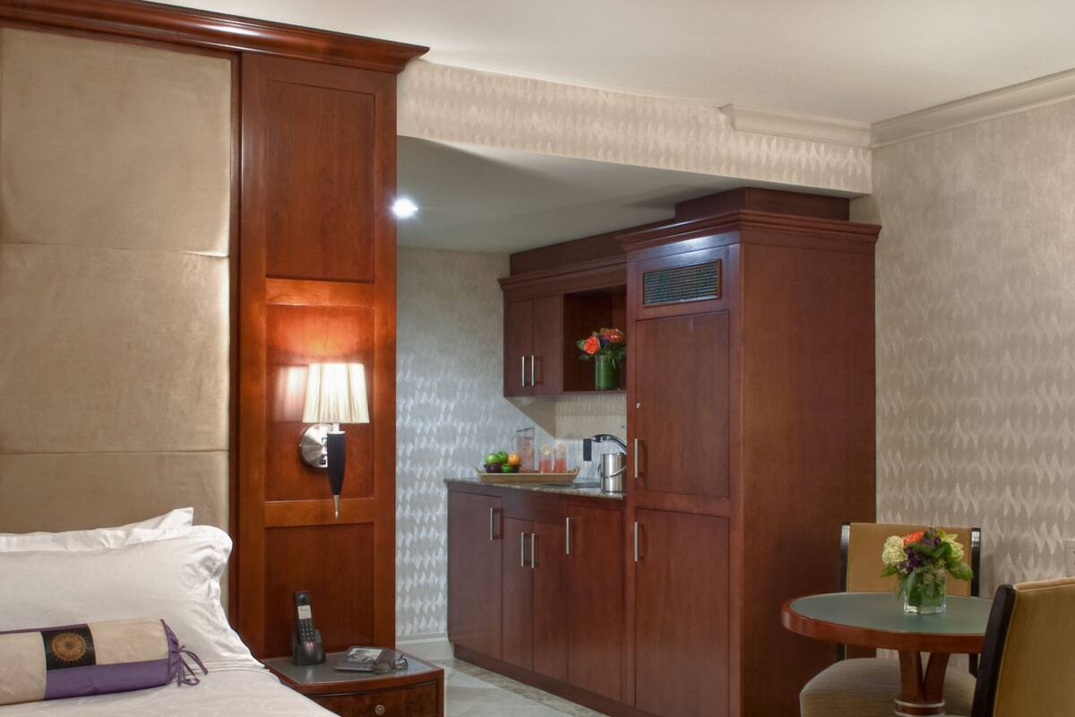 Een hotelkamer met een groot bed, een bureau met lamp, een houten garderobe en een kleine eettafel met stoelen.