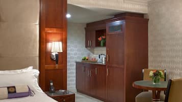 A hotel room with a large bed, a desk with a lamp, a wooden wardrobe, and a small dining table with chairs.