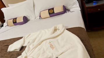 Quarto de hotel com cama bem arrumada, roupão branco com logotipo e almofada com desenho de sol.