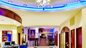 Un hall d’hôtel doté d’une mosaïque circulaire au centre, d’un lustre et d’un escalier menant à un autre niveau.