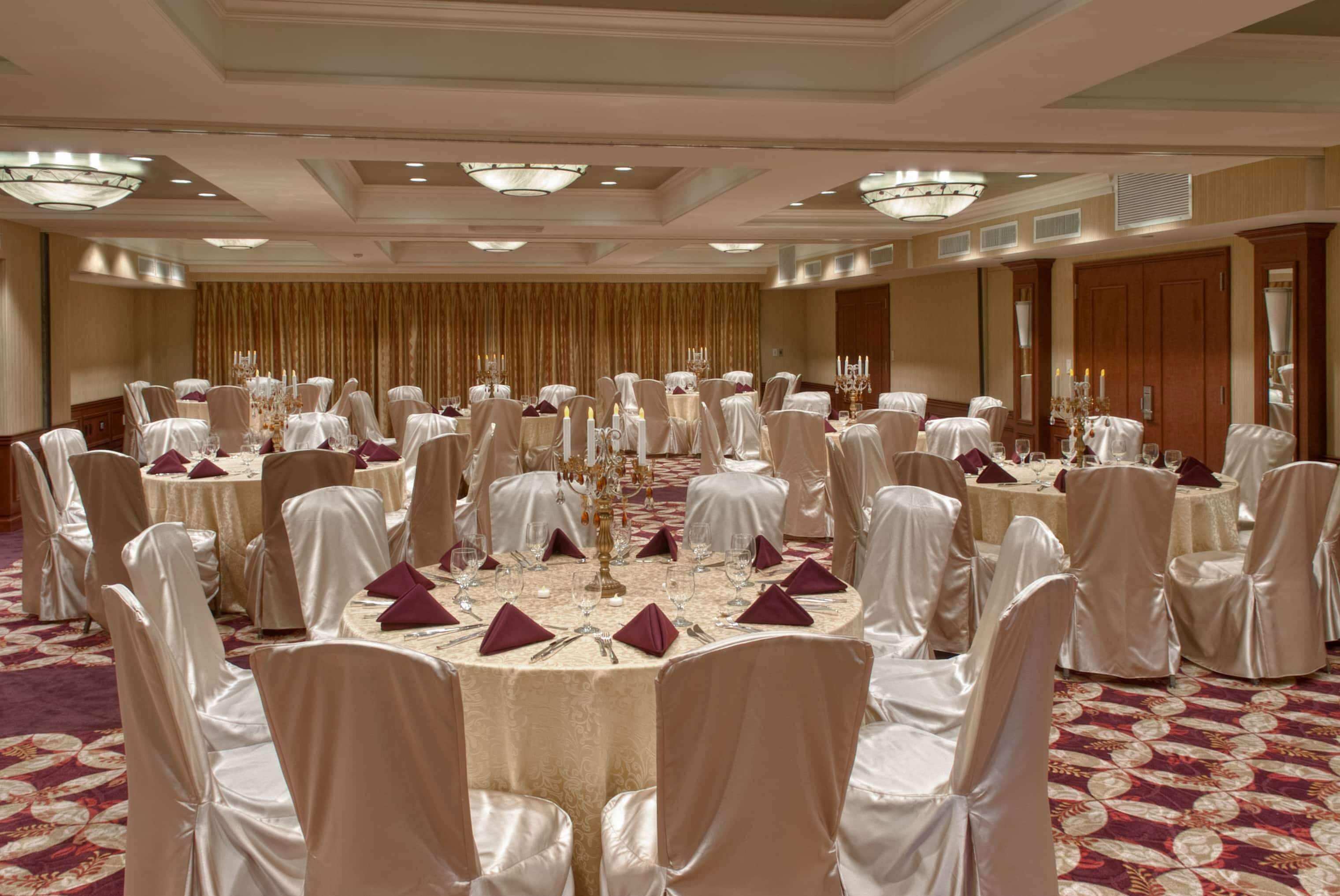A banquet hall with round tables, white chairs, and chandeliers.