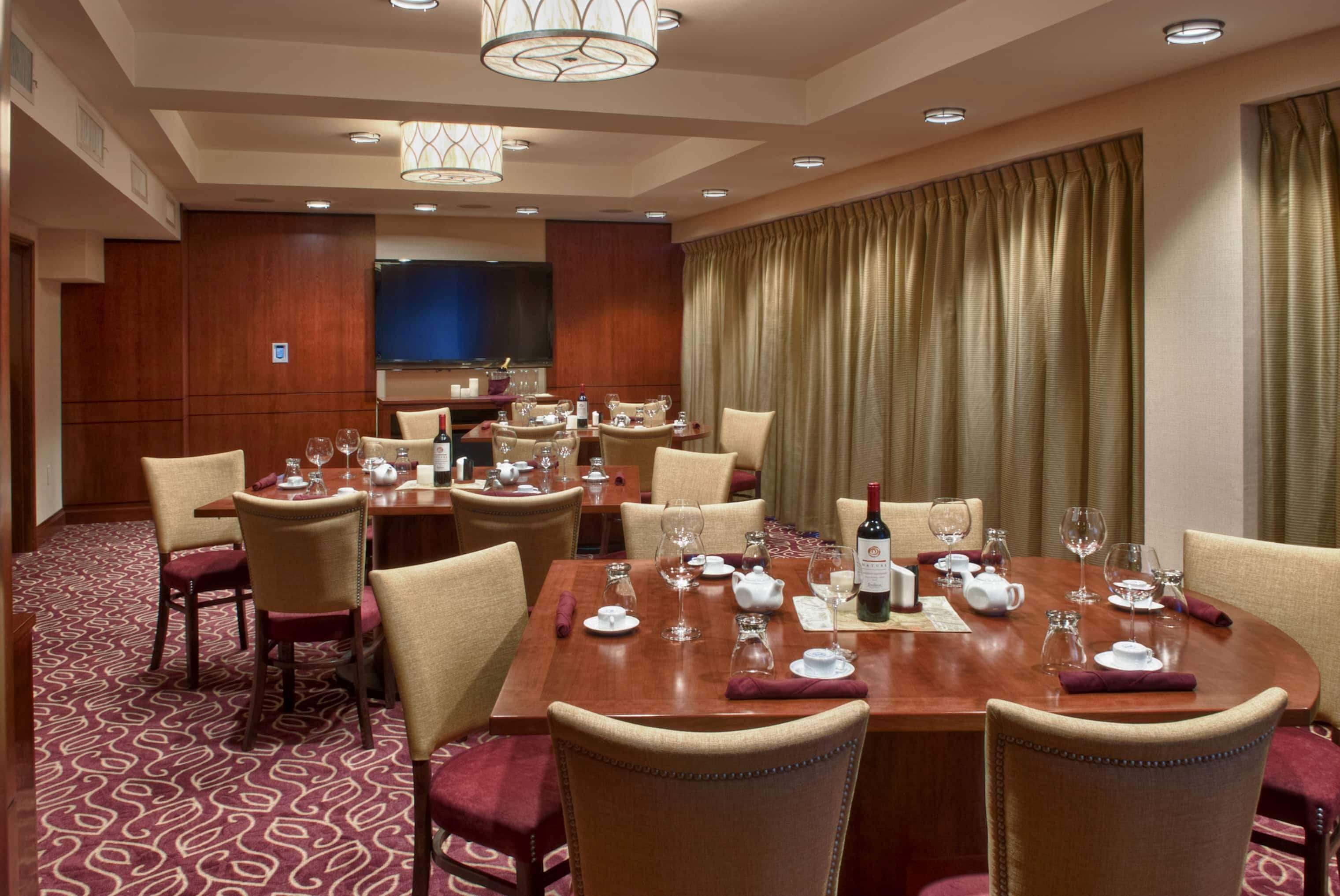 Uma sala de jantar de hotel com várias mesas preparadas para refeições, equipada com cadeiras, copos de vinho e louças.