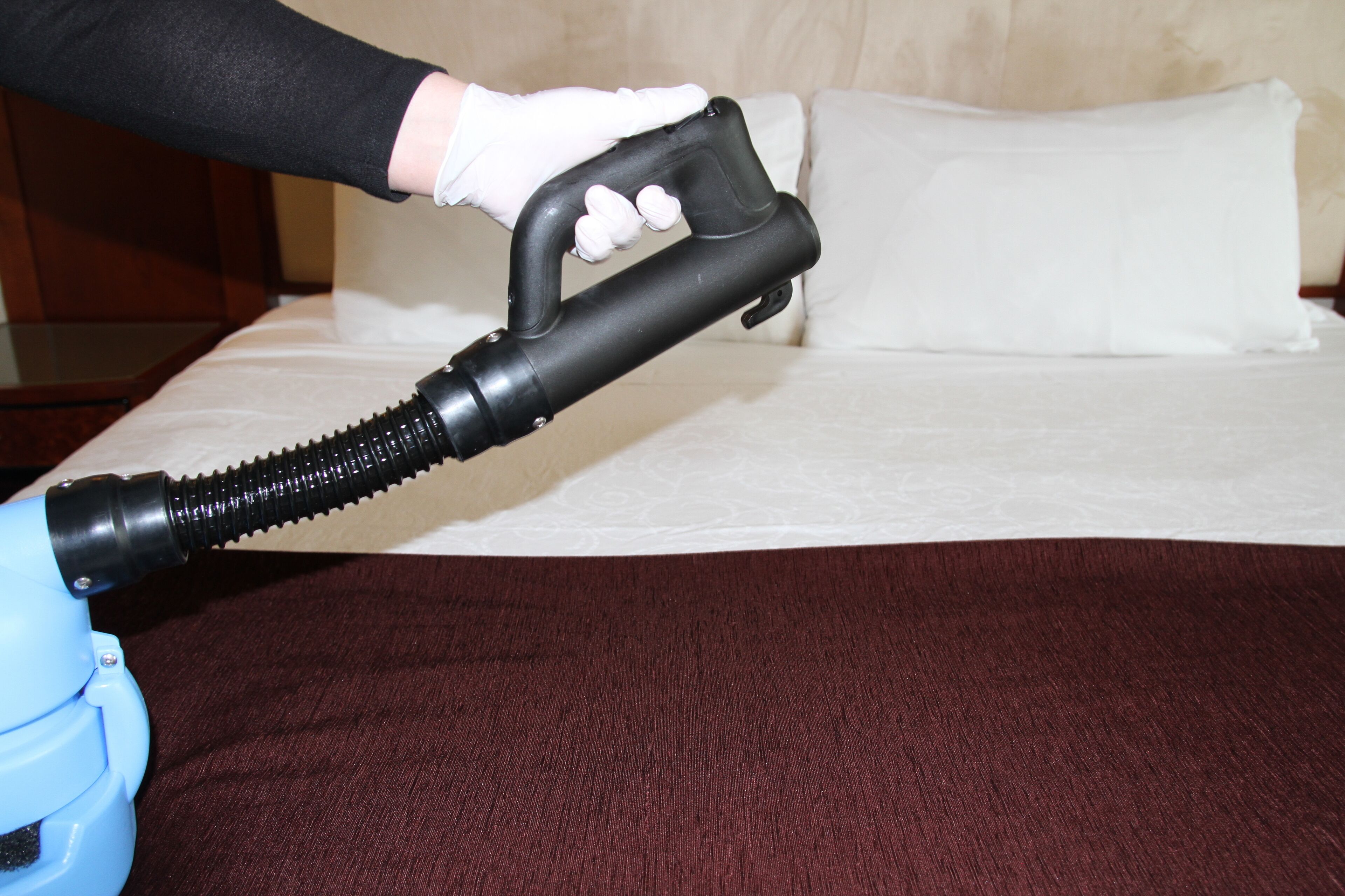 A person using a vacuum cleaner on a bed with a brown cover.