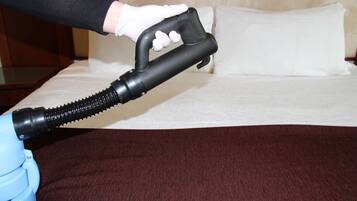 A person using a vacuum cleaner on a bed with a brown cover.