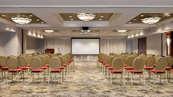 Una sala de conferències amb files de cadires, una pantalla gran i un projector.