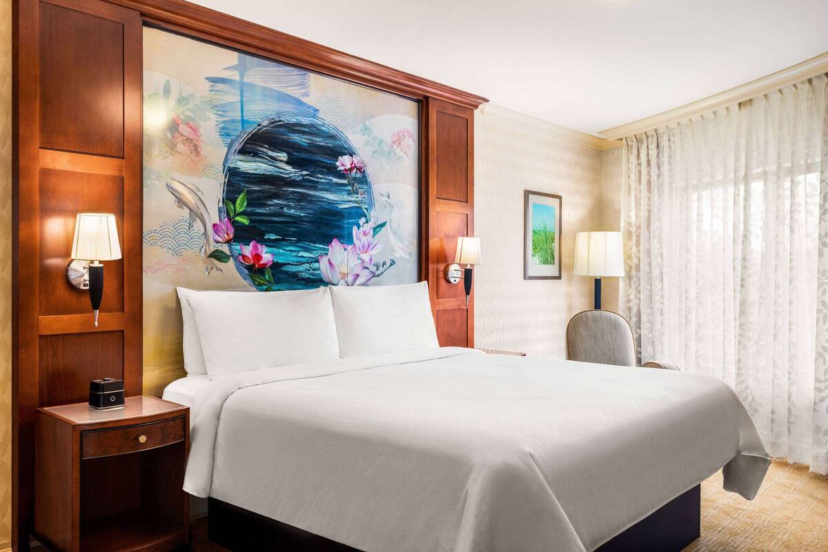 Een hotelkamer met een groot bed, twee nachtkastjes met lampen, een stoel en een schilderij aan de muur.
