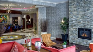 Un hall d’entrée spacieux avec une cheminée en pierre, des canapés rouges, un lustre et un coin repas avec des chaises bleues.
