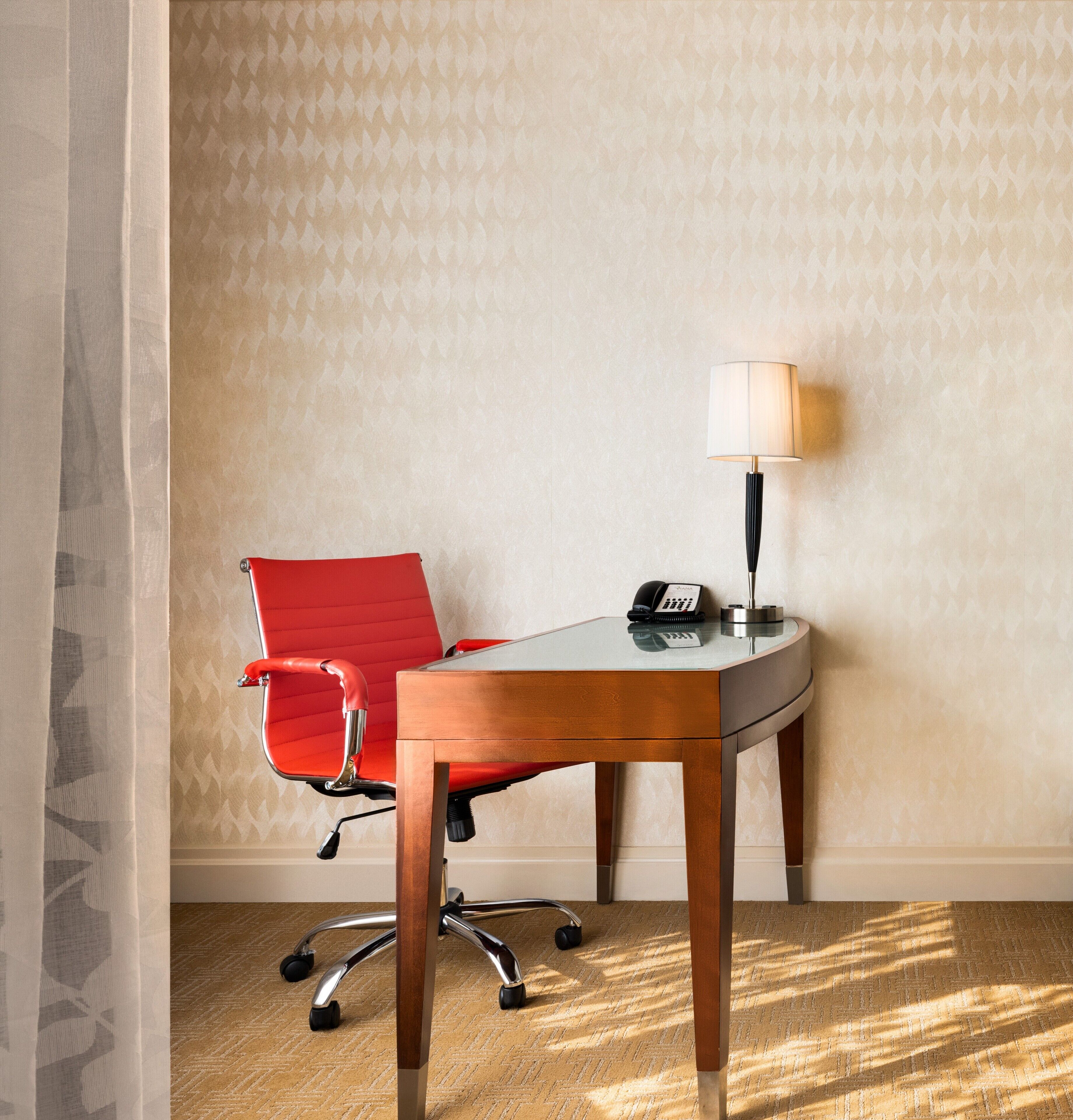 Un bureau d’angle avec un fauteuil de bureau rouge, un bureau, une lampe et un téléphone.