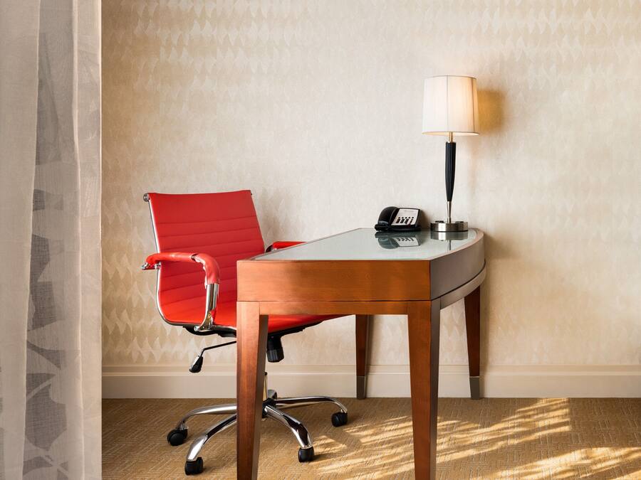 A corner office with a red office chair, a desk, a lamp, and a telephone.