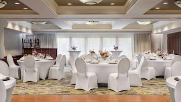 Een feestzaal met ronde tafels, witte stoelen en bloemstukken als decoratie.