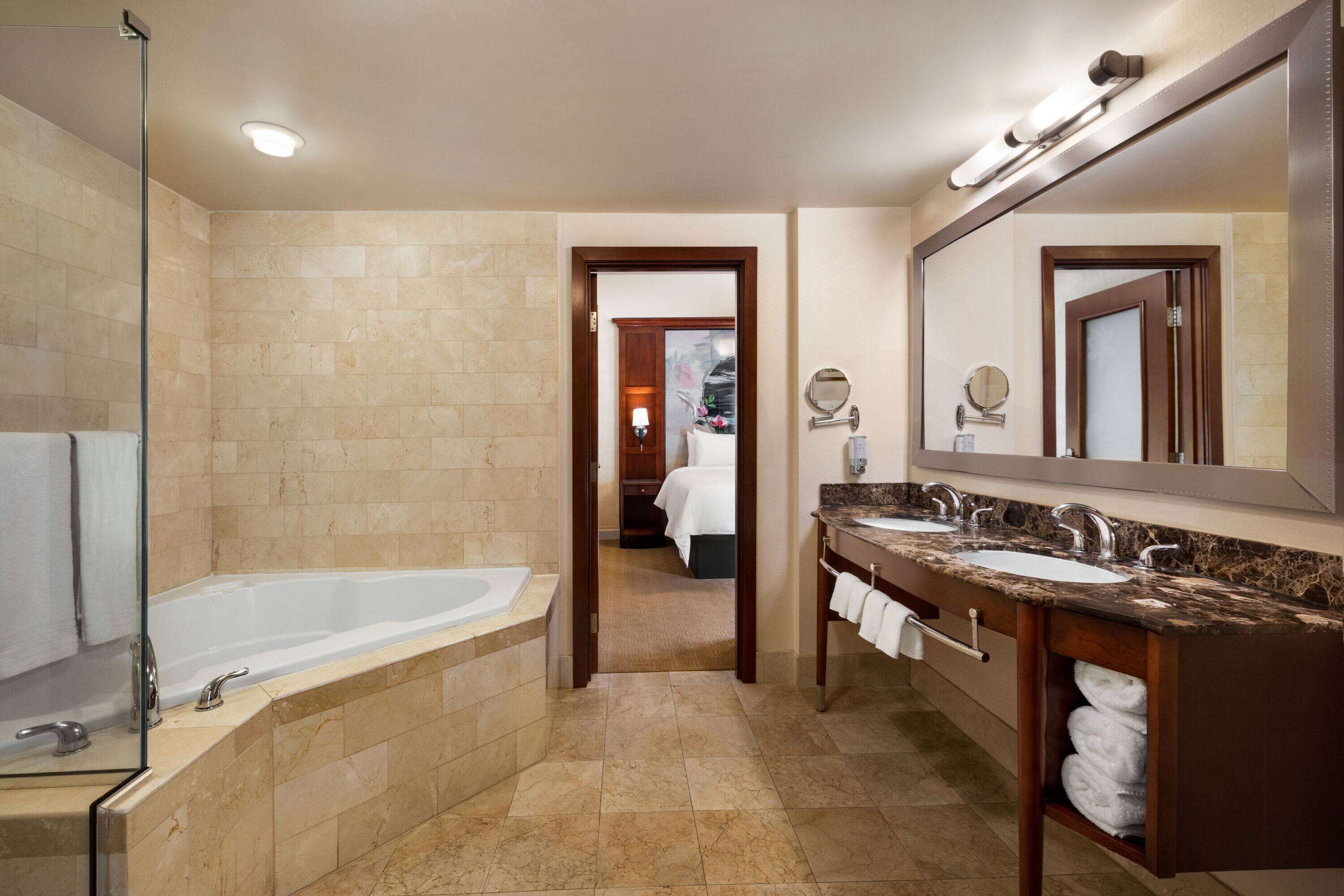 A hotel bathroom with a bathtub, two sinks, and a large mirror.
