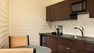 Una cocina compacta con armarios de madera oscura, un microondas integrado, una cafetera y un lavabo.