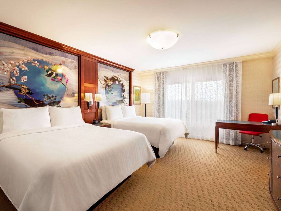Ein Hotelzimmer mit zwei Betten, einem Schreibtisch, einem Sessel, einem Fernseher und Bildern an der Wand.
