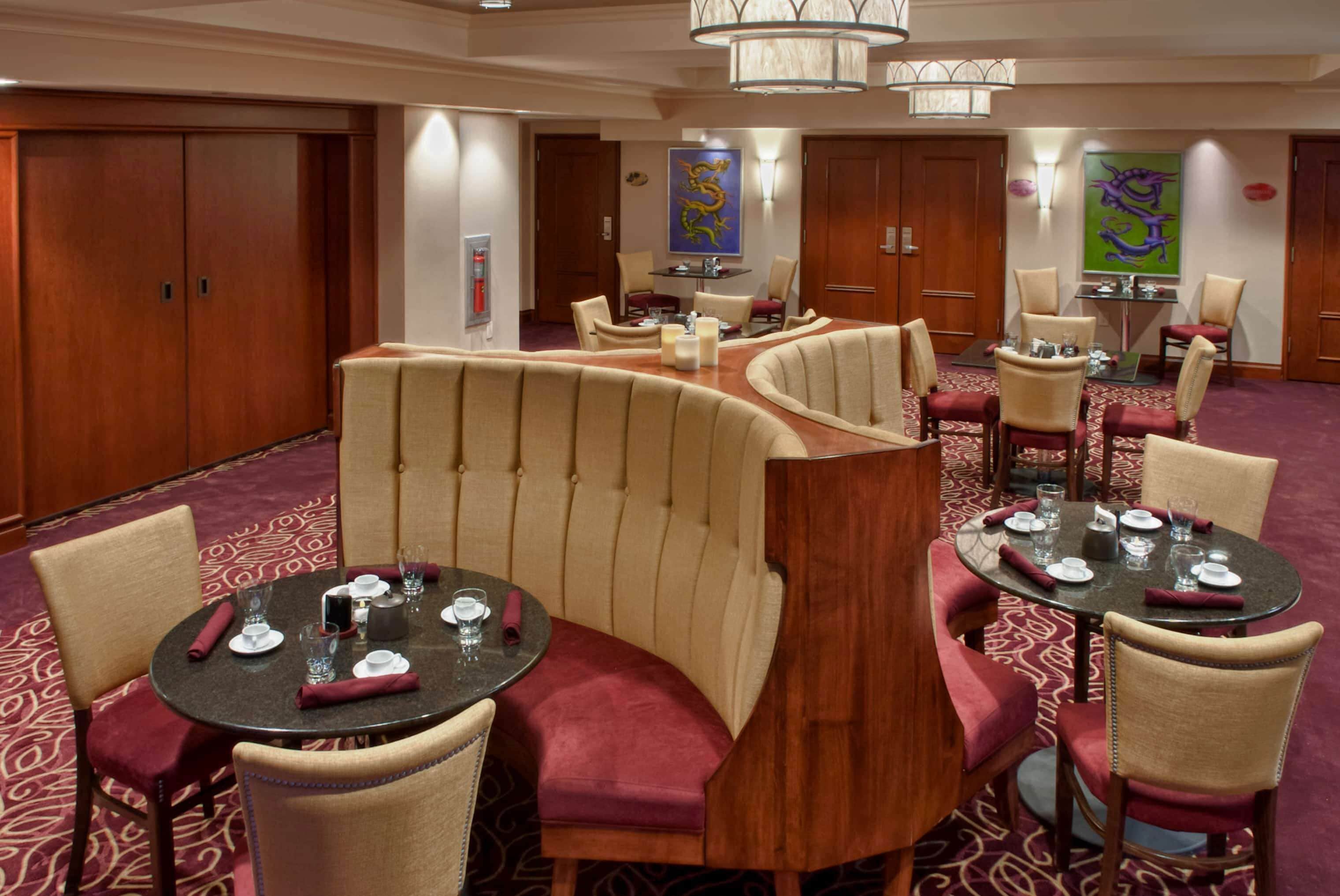A hotel dining area with round tables, cushioned booths, and a patterned carpet.
