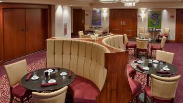 A hotel dining area with round tables, cushioned booths, and a patterned carpet.