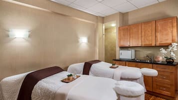 A hotel room with two beds, a small kitchenette, and a bathroom.