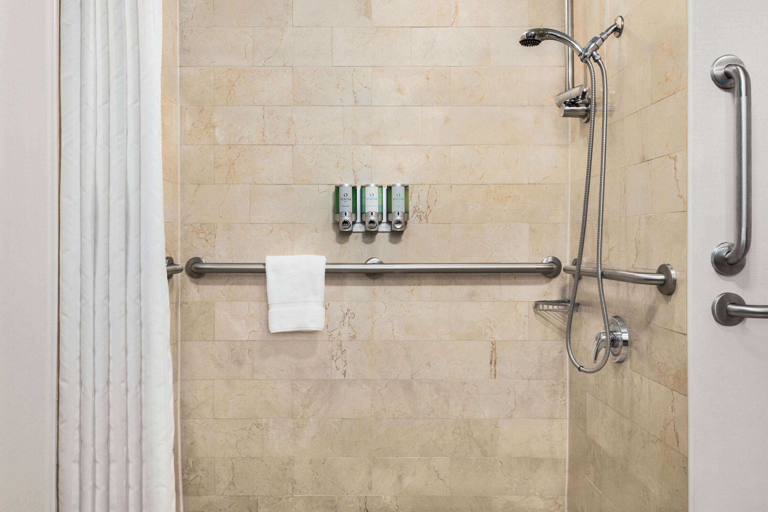 A shower area with a grab bar, a towel rack, and a wall-mounted soap dispenser.