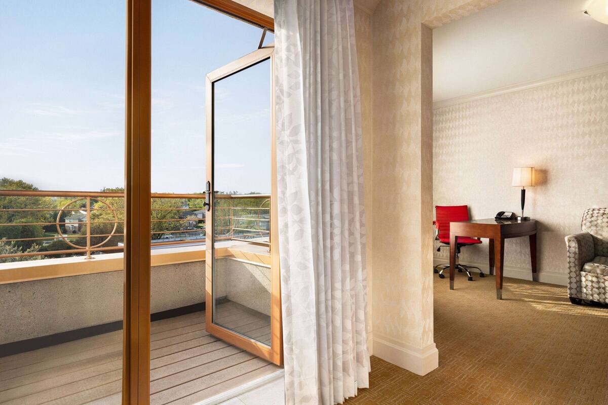 Een hotelkamer met balkon, bureau, stoel en lamp.