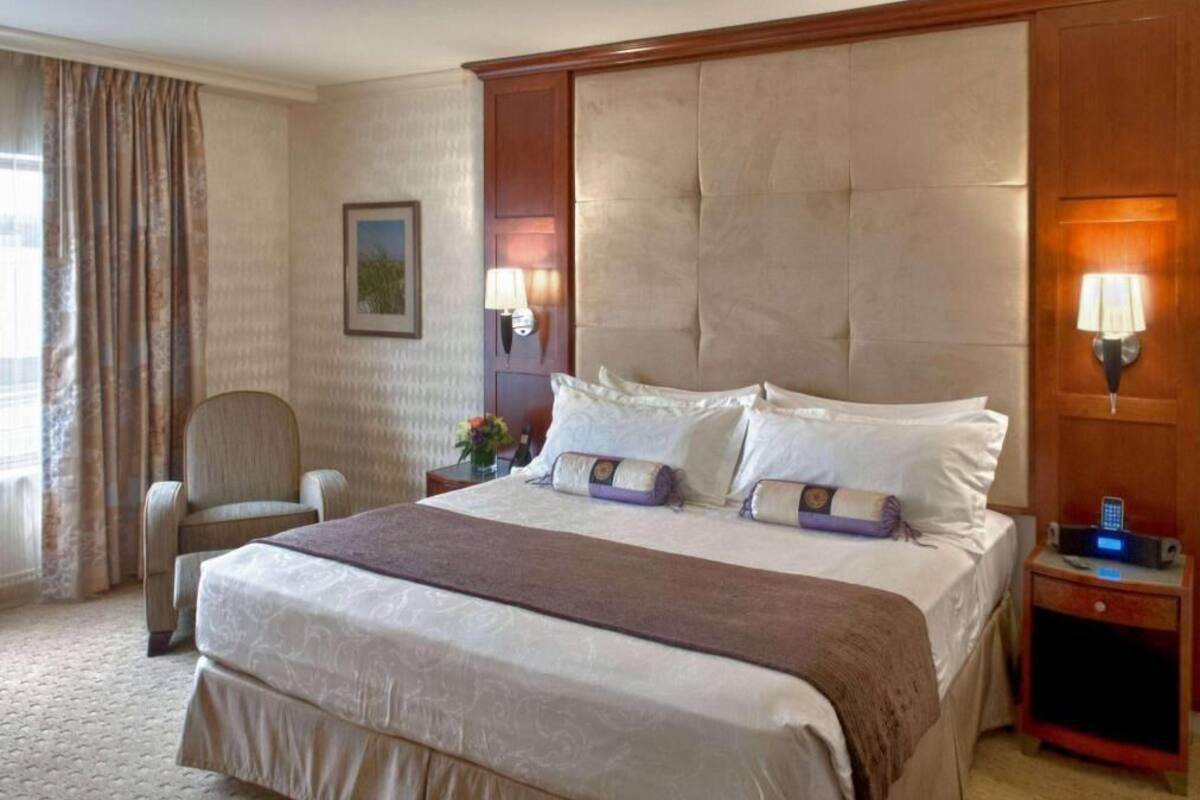 Een hotelkamer met een groot bed, een stoel, een nachtkastje met een lamp en een wandlamp.