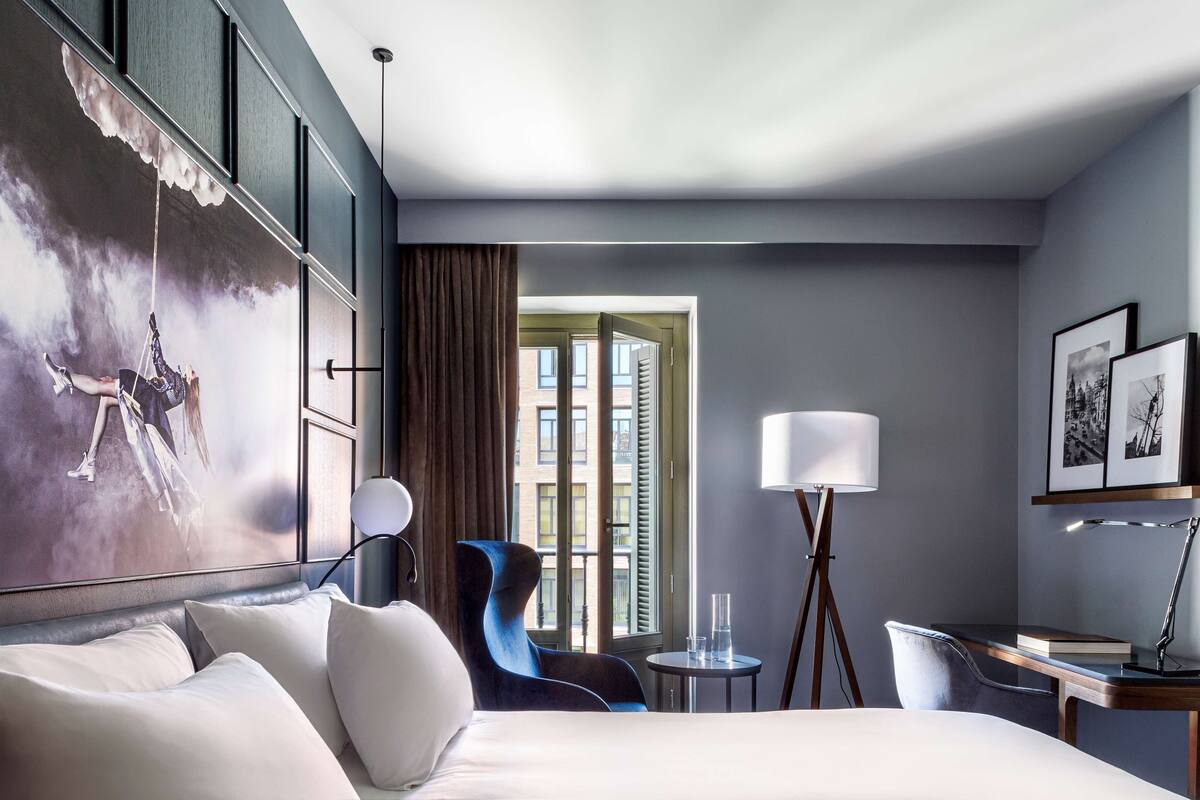 Camera d'albergo con un letto grande, una scrivania, una sedia, una lampada e vista sull'esterno.