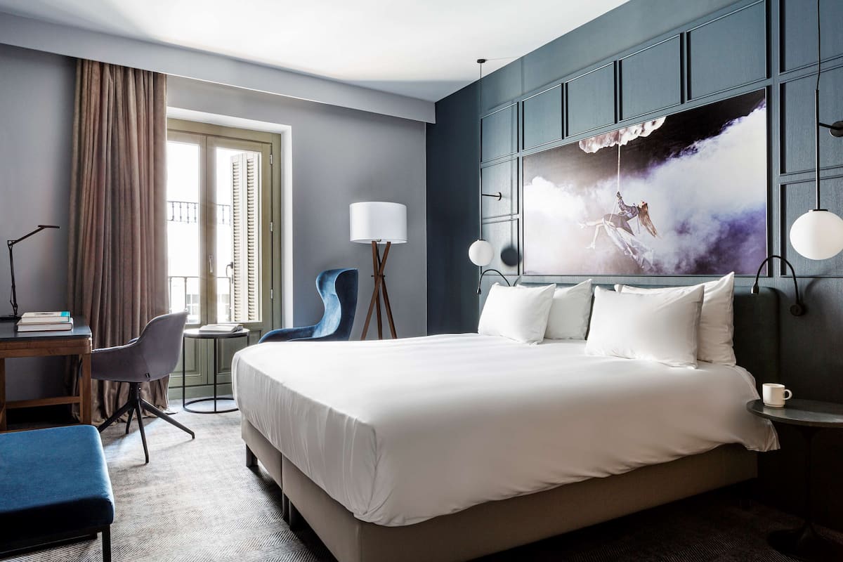 Una camera d'albergo con un letto grande, una scrivania con una sedia, un tavolino e un'ampia finestra con tende.