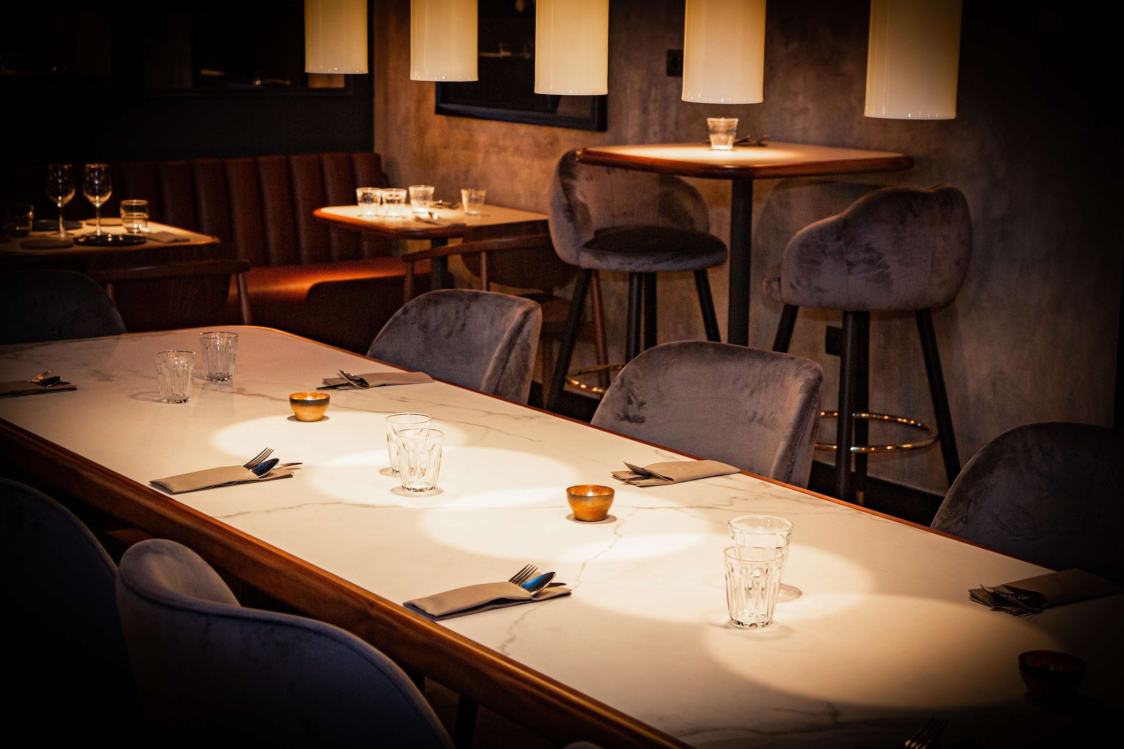 Un restaurante con una larga mesa de comedor, numerosas sillas y algunas mesas con lámparas.