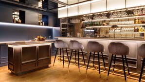 Un área de bar con taburetes, una barra y estantes con botellas y vasos.