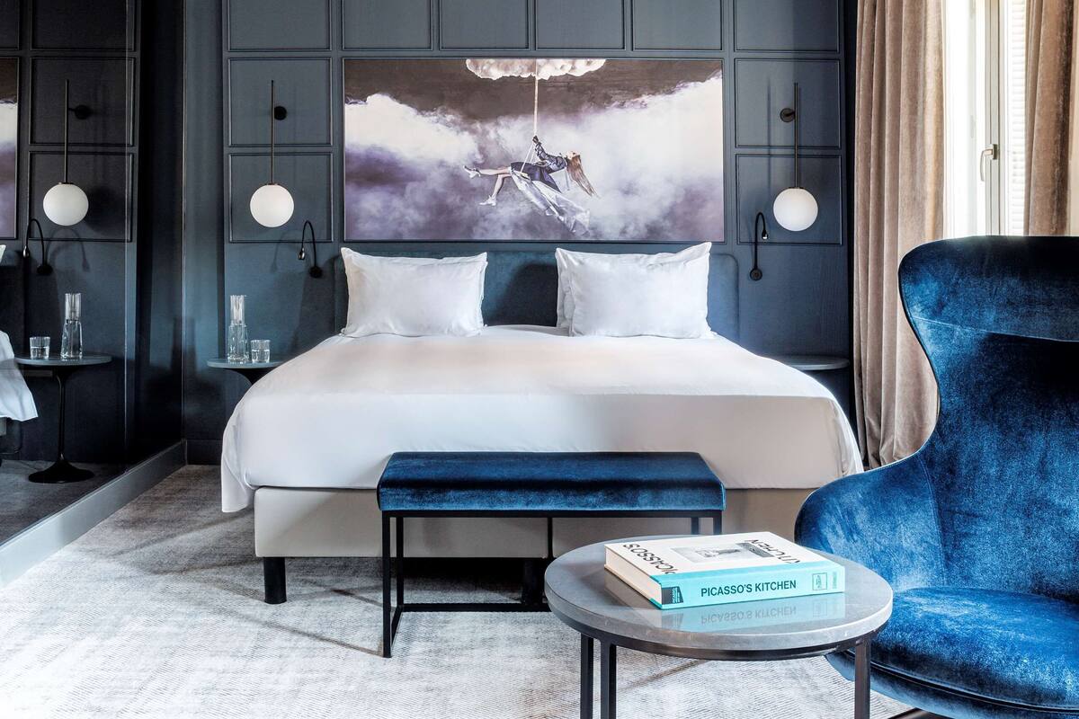 Una camera d'albergo moderna con un grande letto, una poltrona blu e un quadro appeso al muro.