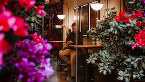 Una persona sentada a una mesa dentro de un restaurante con un separador de vidrio.