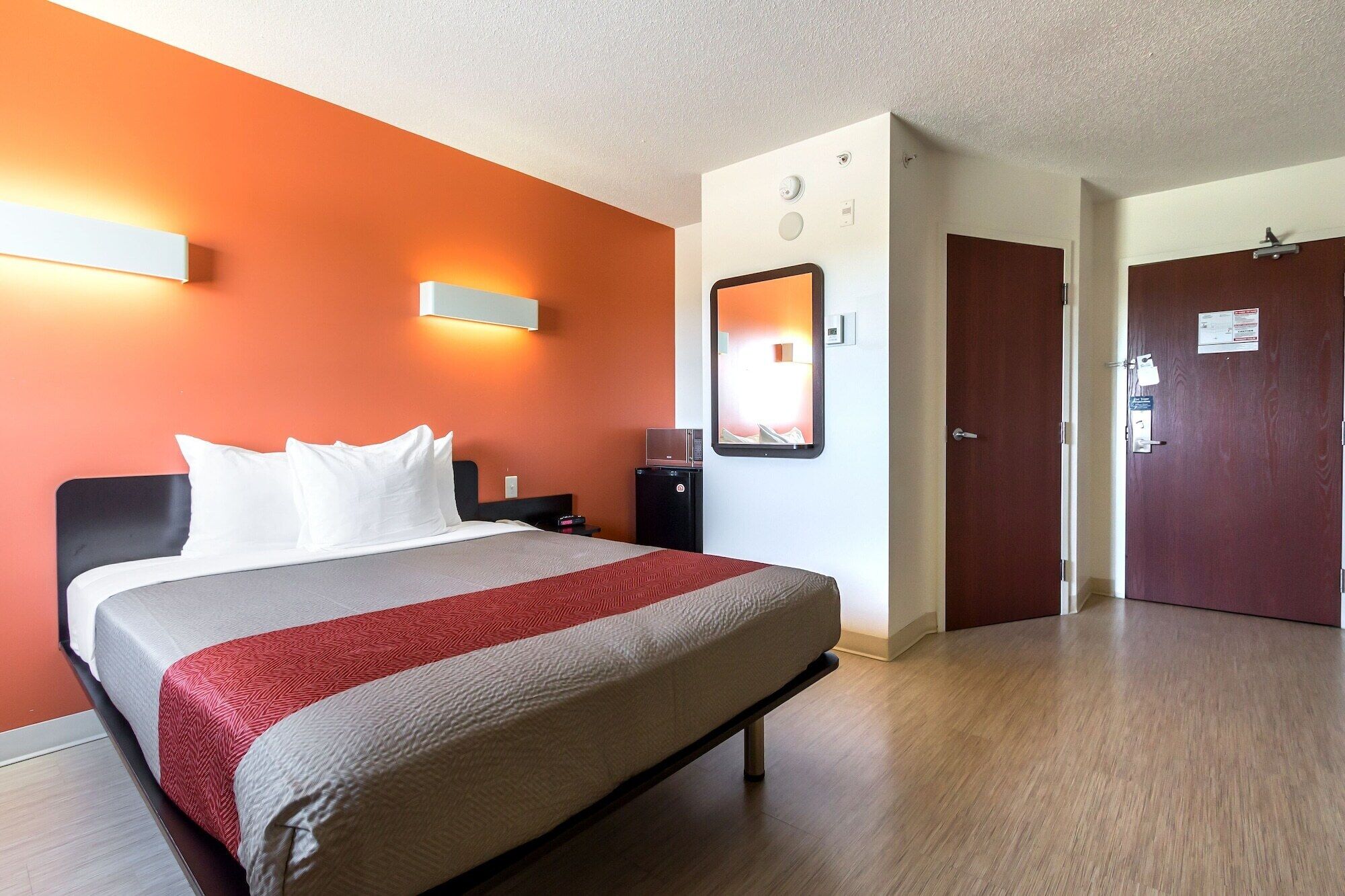 Een hotelkamer met een bed, een bureau, een stoel, een spiegel en een deur.