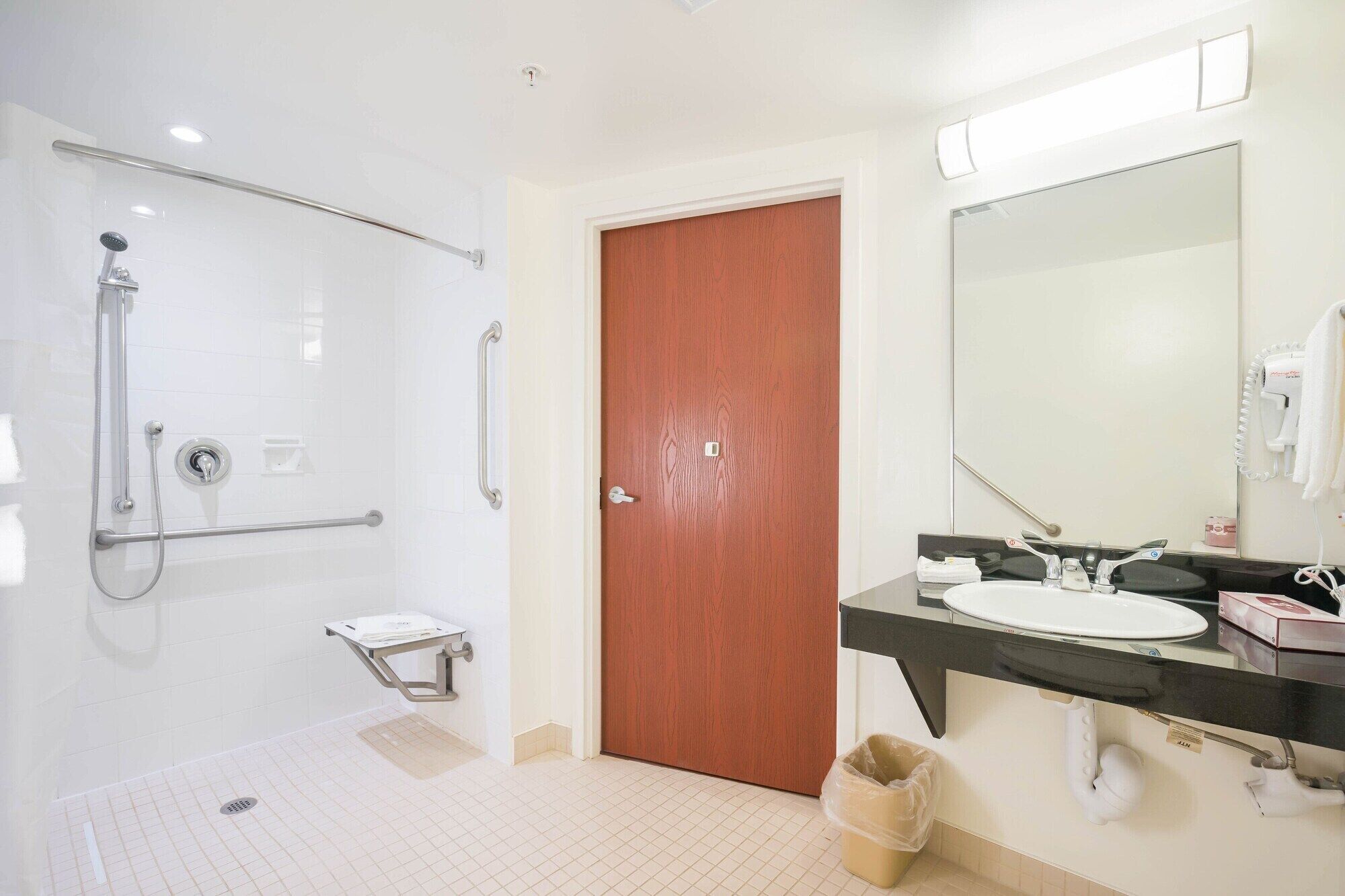 A modern bathroom with a glass-enclosed shower, a wooden door, a sink with a mirror, and a towel rack.