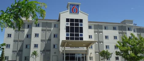 Un hotel de varios pisos con un llamativo letrero con el número '6', amplias ventanas y una entrada cubierta.