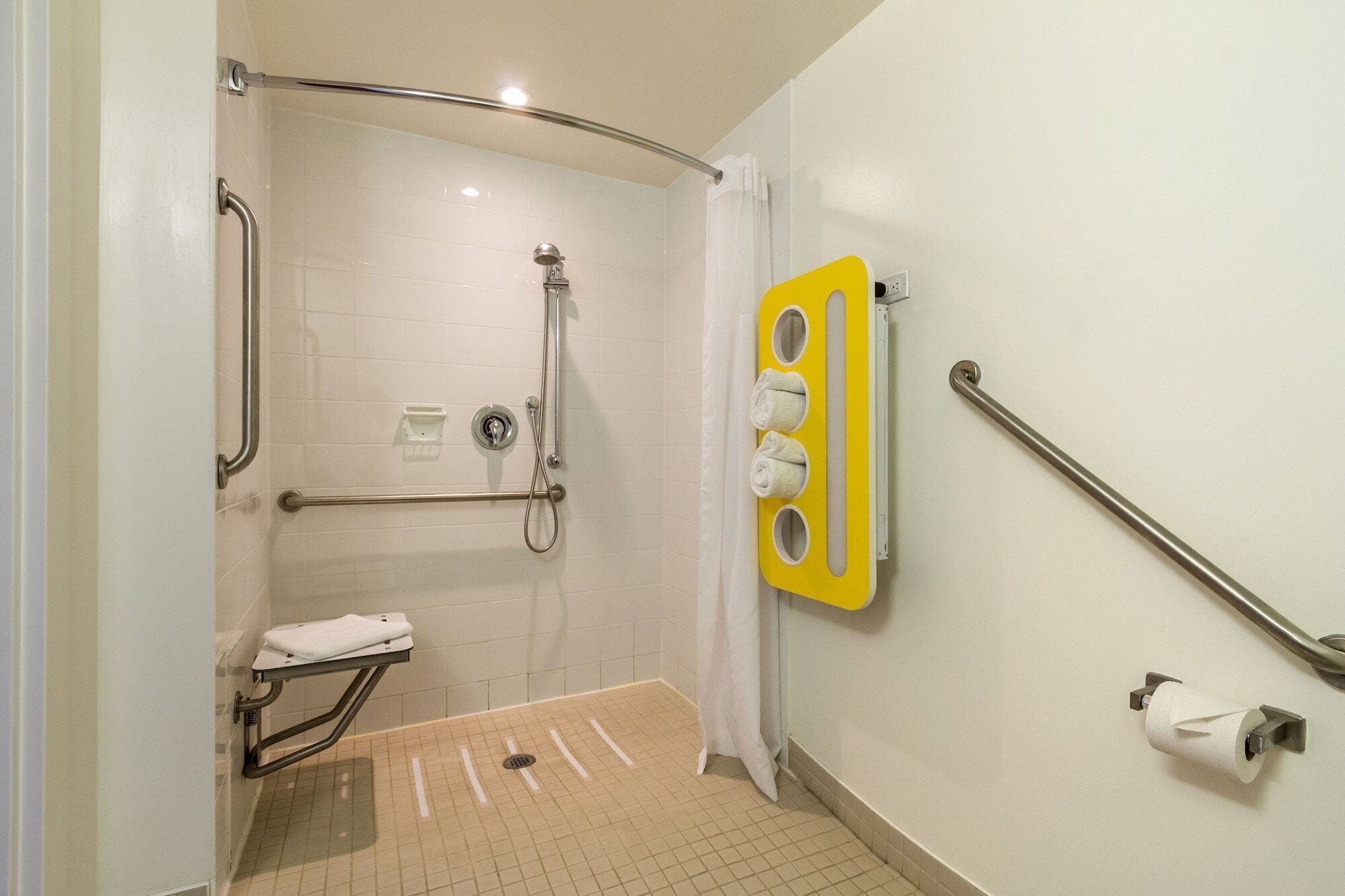 Baño con ducha, barras de apoyo, toallero y soporte para papel higiénico.