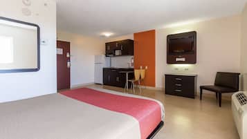 A hotel room with a bed, a desk, a kitchenette, a TV, and a heater.