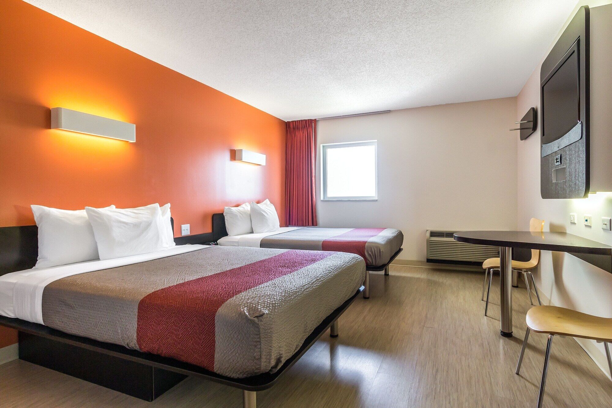 A hotel room with two beds, a desk, and a TV.