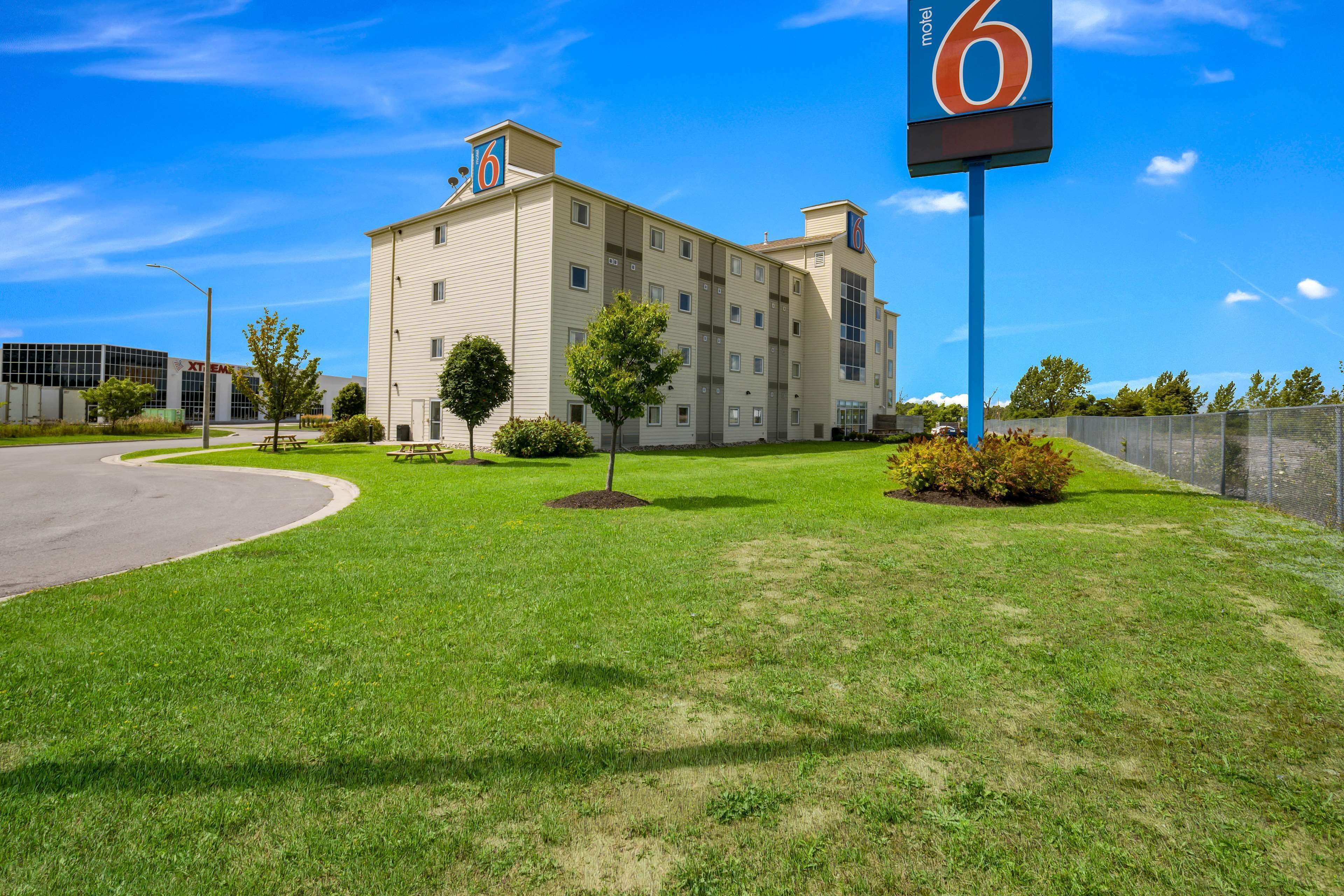 A motel with a large sign displaying the number 6, a well-maintained lawn, and a building with multiple windows and a flat roof.