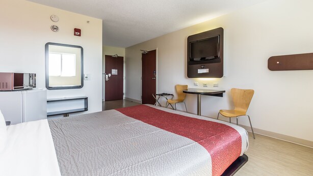 Una habitación de hotel con cama, escritorio, dos sillas, televisor y espejo.