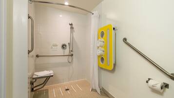 A bathroom with a shower, grab bars, a wheelchair-accessible bench, and a toilet paper holder.
