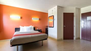 A hotel room with a bed, a nightstand, a wall-mounted mirror, and a door.