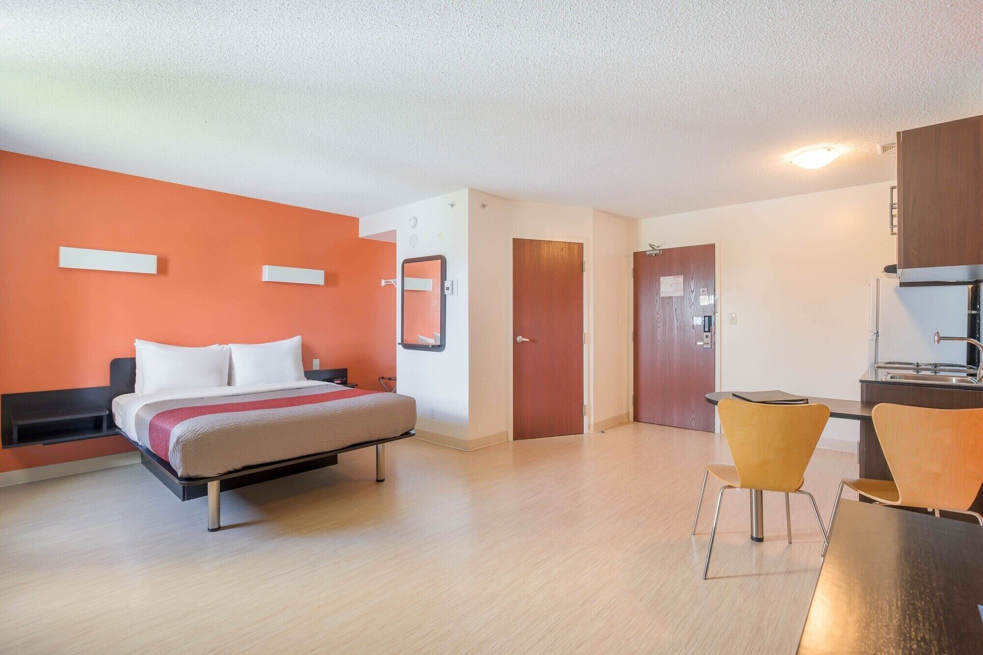 A hotel room with a bed, a desk, a chair, and a kitchenette.