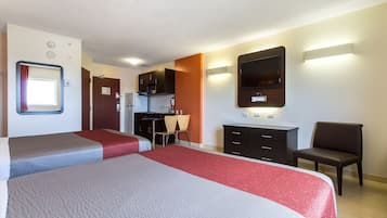 Een hotelkamer met twee bedden, een kitchenette, een televisie en een stoel.