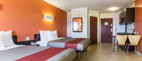 A hotel room with two beds, a small kitchenette, and a dining area with two chairs.
