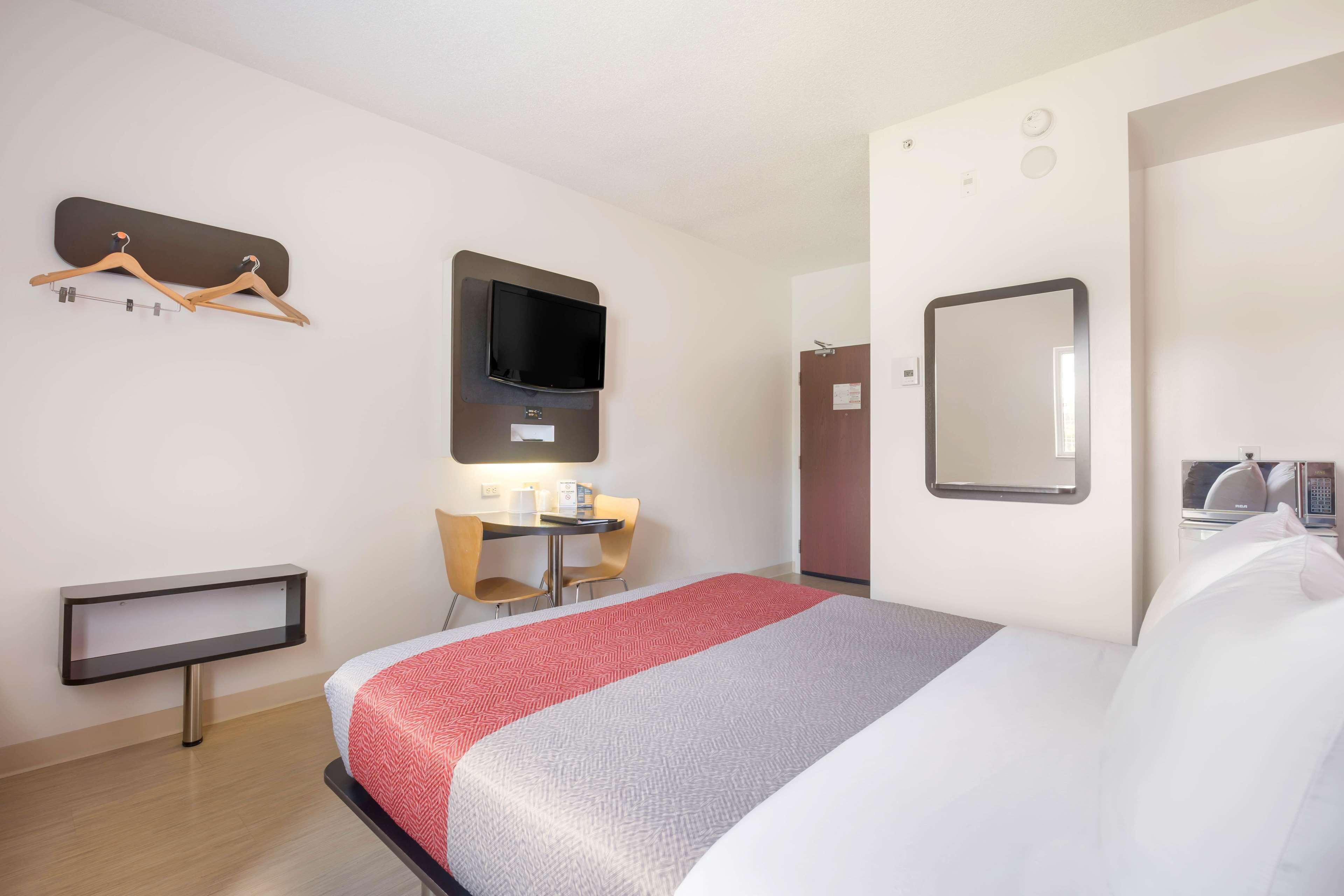 Une chambre d’hôtel équipée d’un lit, d’un bureau, d’une chaise, d’une télévision, d’un miroir et d’un porte-manteau.
