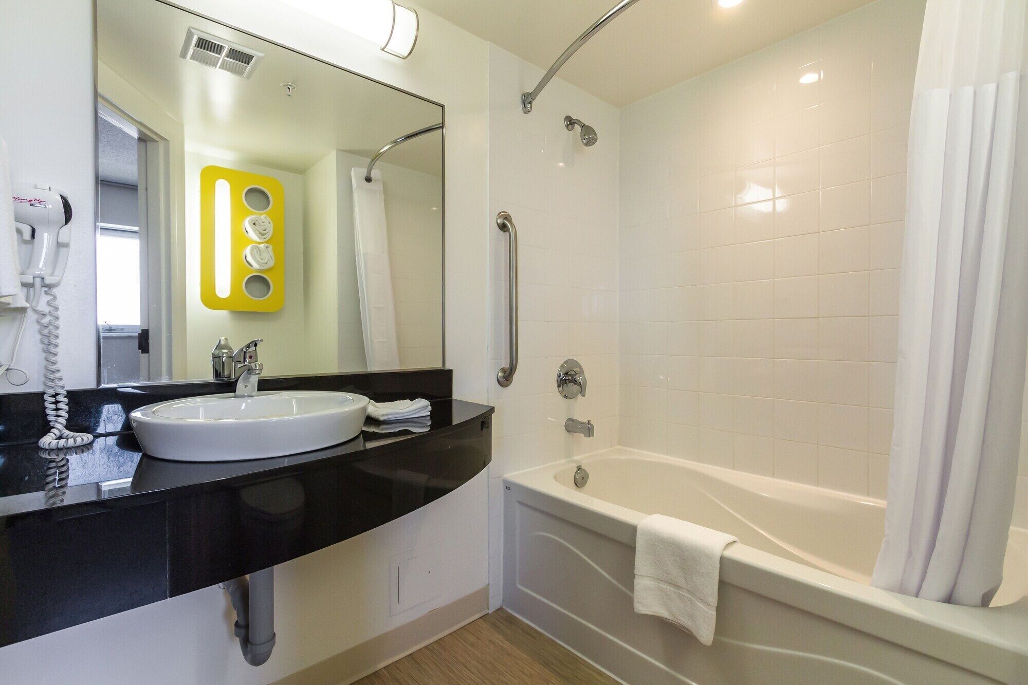 Un baño moderno con un lavamanos blanco, encimera negra y bañera blanca.